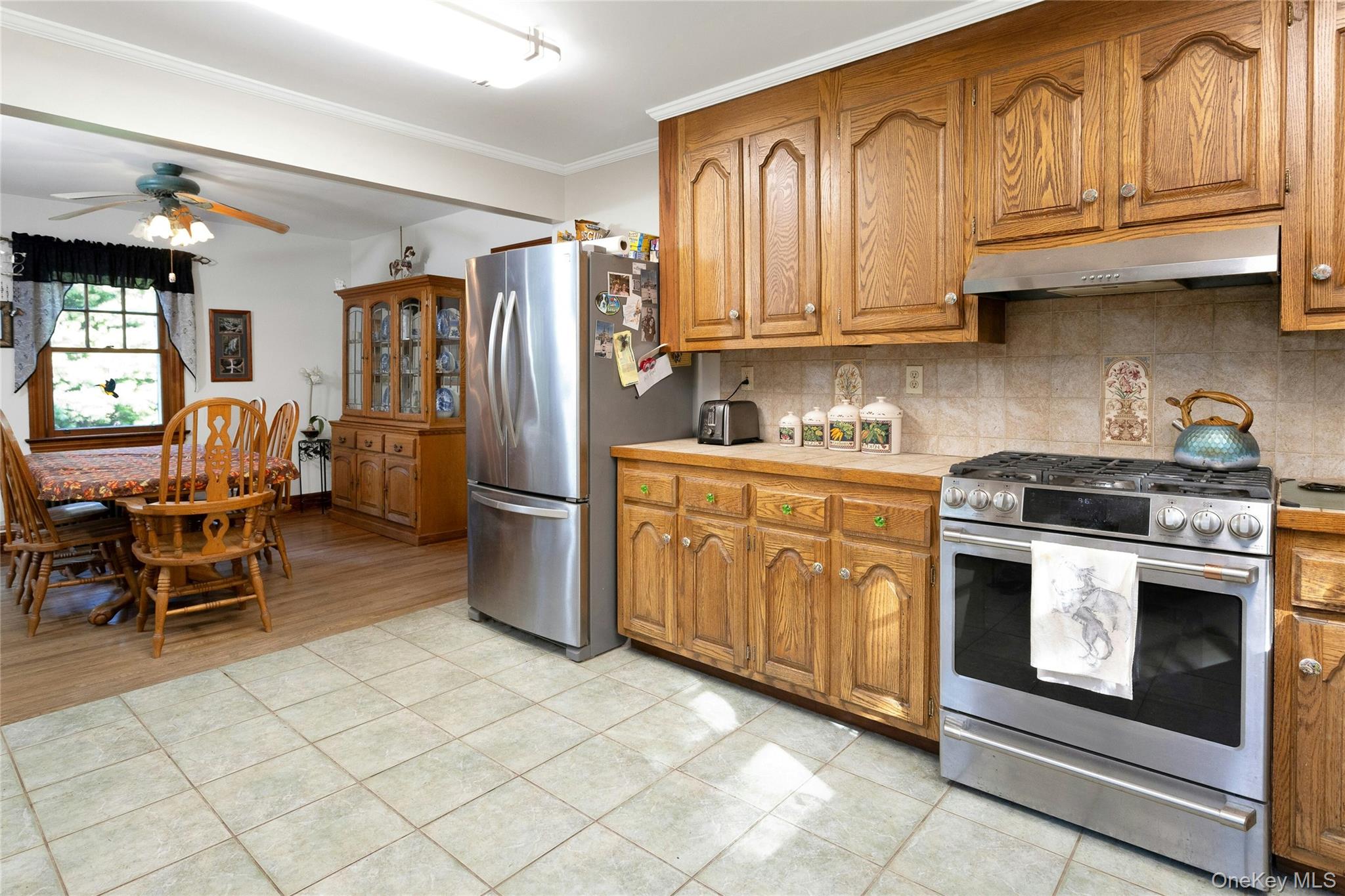 73 Lake Ellis Road Wingdale, NY 12594 - Photo 6 of 41 Kitchen with stainless steel appliances, decorative backsplash, brown cabinetry, a ceiling fan, and crown molding