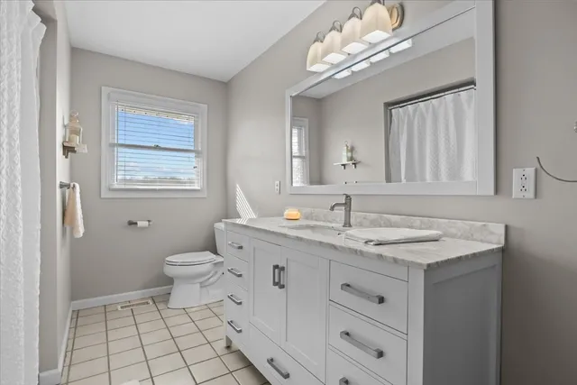 a bathroom with a granite countertop sink a toilet a mirror and a window