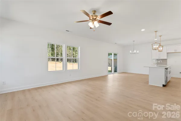 an empty room with chandelier fan and windows
