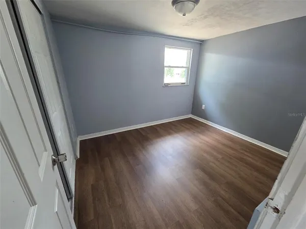 a view of an empty room with wooden floor and a window