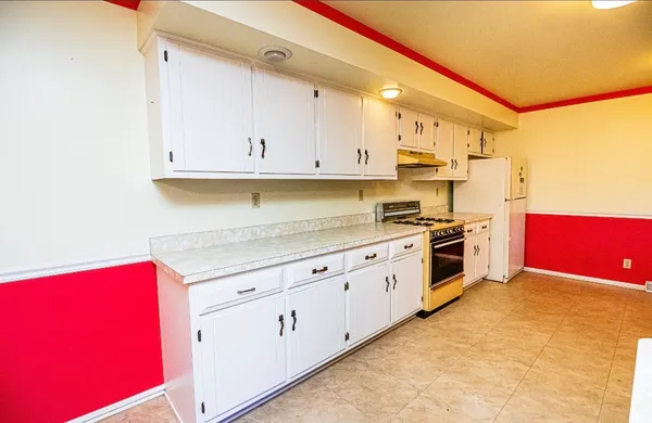 a kitchen with granite countertop a refrigerator a stove and white cabinets