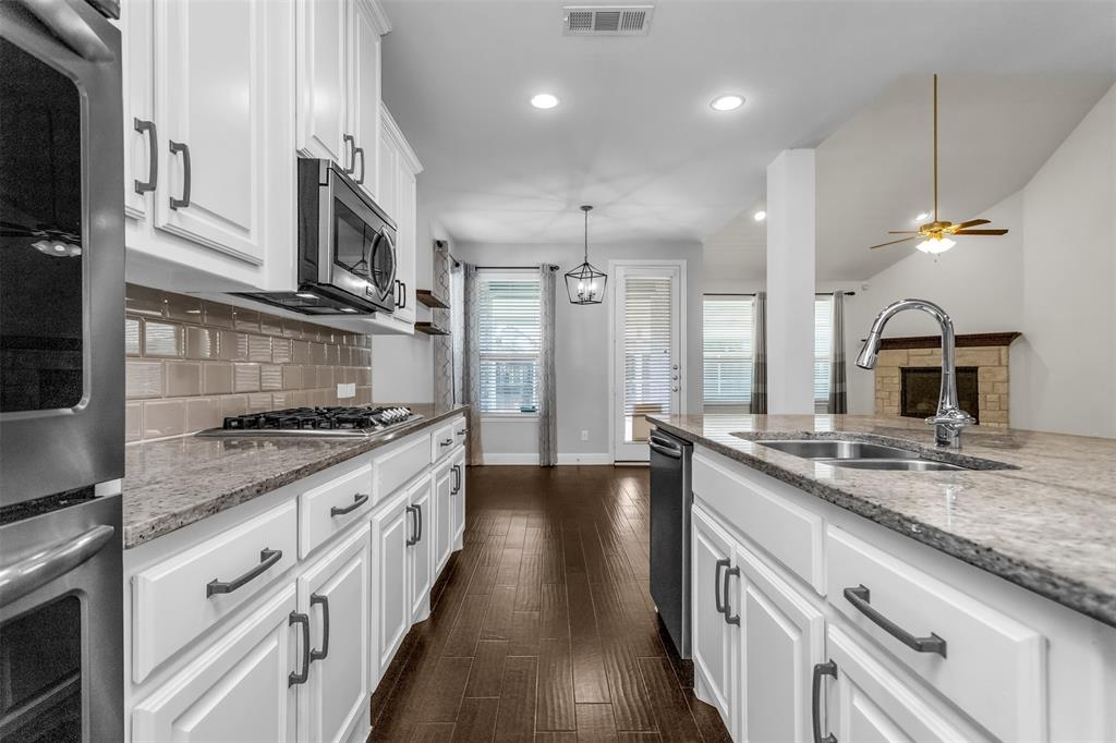 15713 Canyon Ridge Prosper, TX 75078 - Photo 18 of 38 Kitchen showcasing white cabinetry with dark hardware, granite countertops, subway tile backsplash, and stainless steel appliances including an oven, microwave, and dishwasher