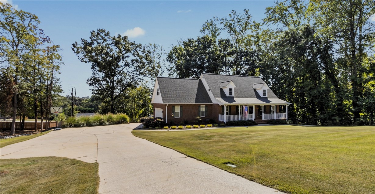 Mature trees frame a welcoming front porch and concrete driveway leading to this traditional brick home.