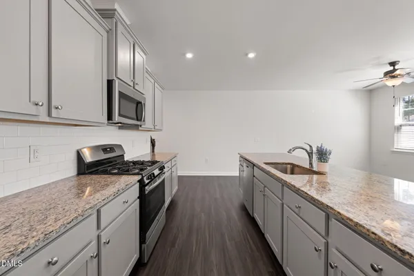 a kitchen with granite countertop stainless steel appliances a sink a stove top oven a counter space and cabinets