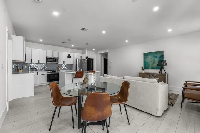 a kitchen with stainless steel appliances kitchen island granite countertop a dining table chairs and a refrigerator