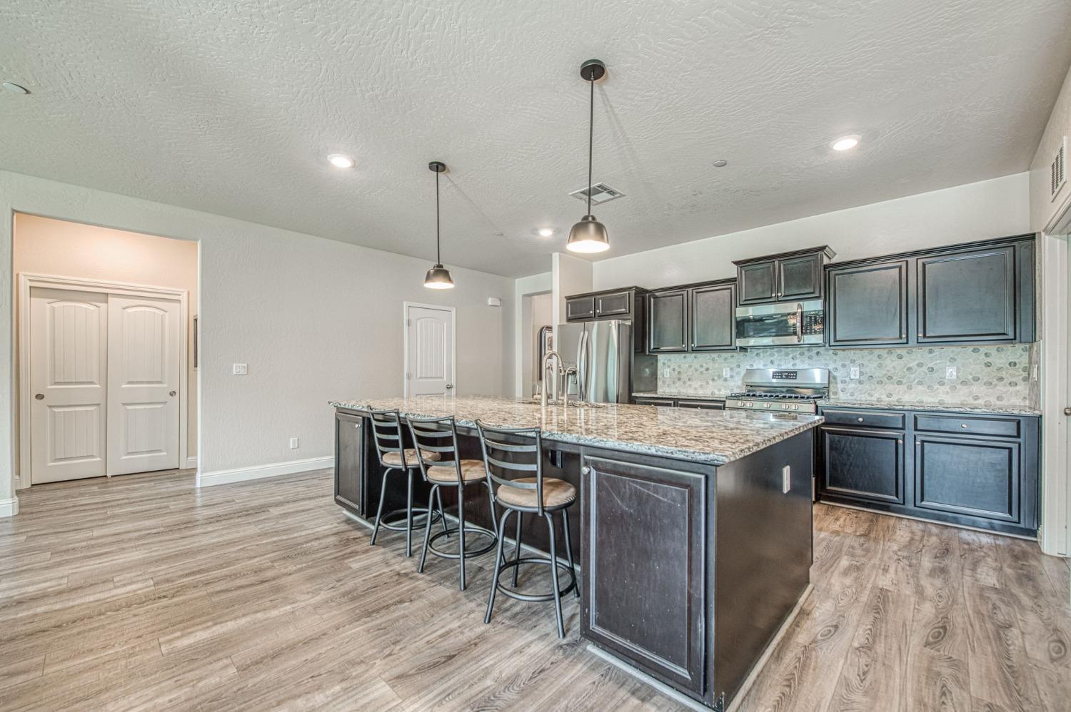 574 Expedition Way Madera, CA 93636 - Photo 11 of 26 a kitchen with stainless steel appliances granite countertop a table chairs and a wooden floors