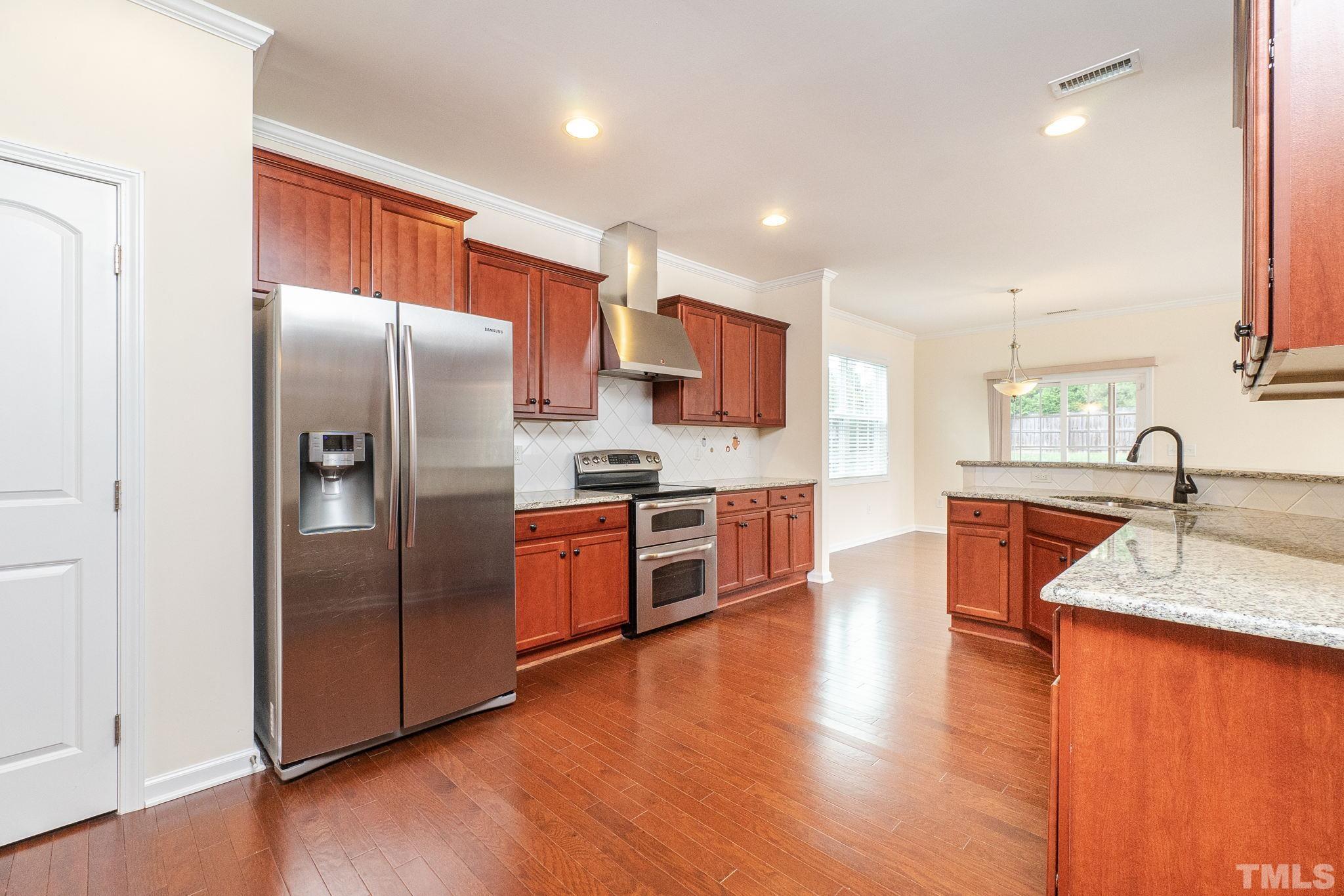 222 Strolling Way Durham, NC 27707 - Photo 7 of 26 a large kitchen with stainless steel appliances granite countertop a refrigerator a sink a stove and a wooden floors