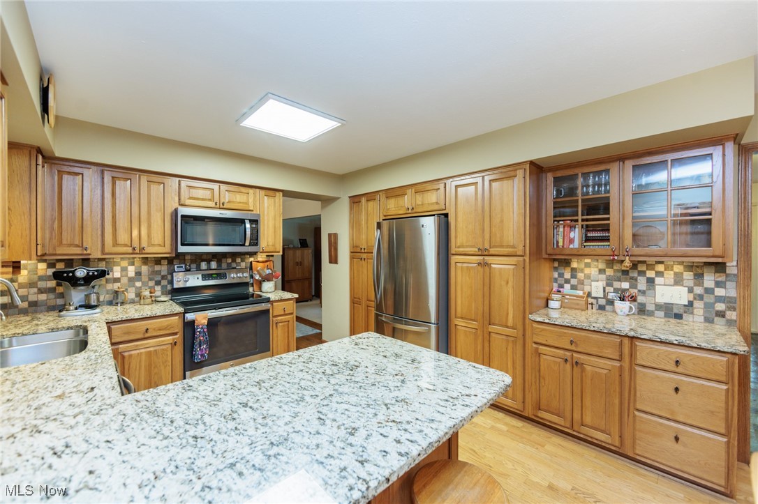 37451 Hunters Ridge Solon, OH 44139 - Photo 12 of 42 Kitchen featuring decorative backsplash, appliances with stainless steel finishes, light wood-type flooring, light stone countertops, and glass insert cabinets