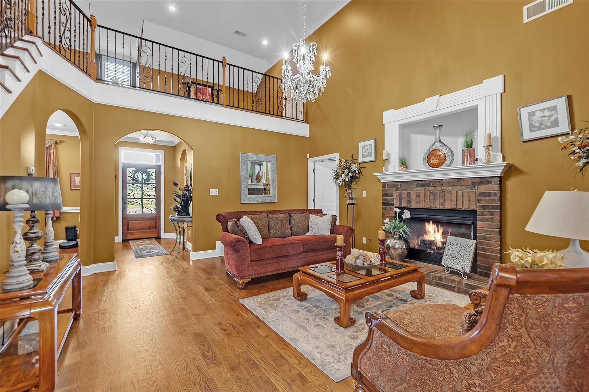 7284 Bucknell Road Millington, TN 38053 - Photo 7 of 35 Two-story living area featuring hardwood flooring, a brick fireplace with a white mantel, and a grand chandelier