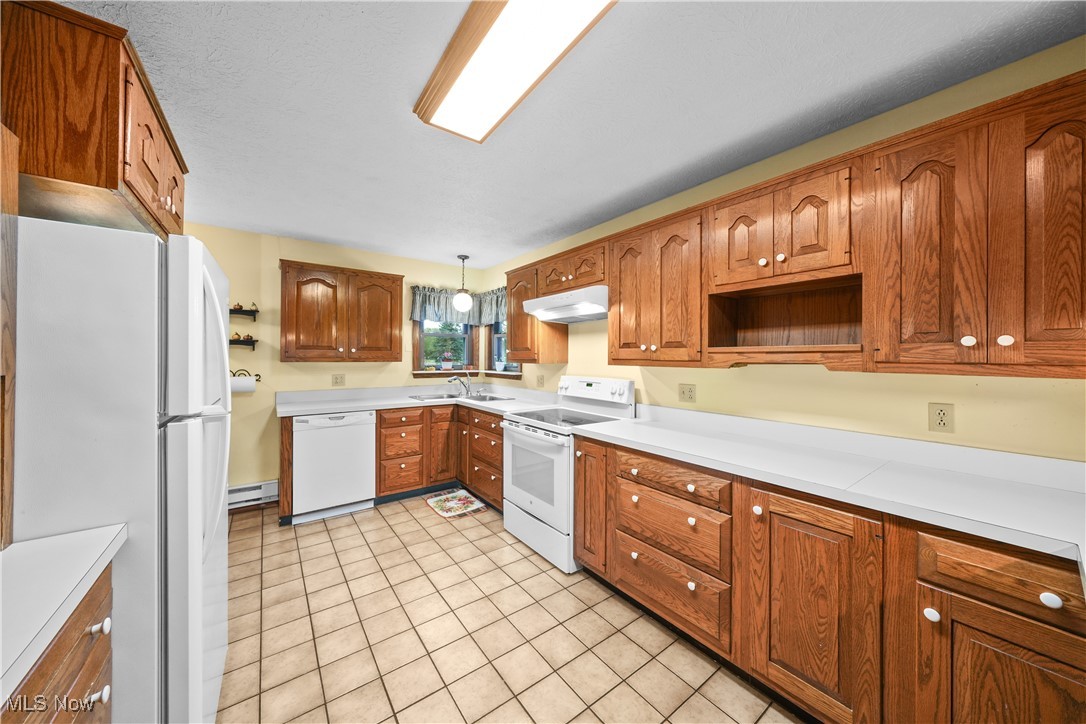 10 Kehner Road Mogadore, OH 44260 - Photo 7 of 32 Kitchen with hanging light fixtures, light tile patterned flooring, white appliances, a baseboard radiator, and sink