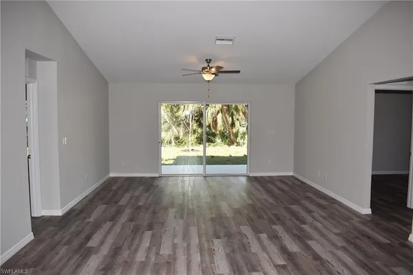an empty room with wooden floor chandelier fan and windows