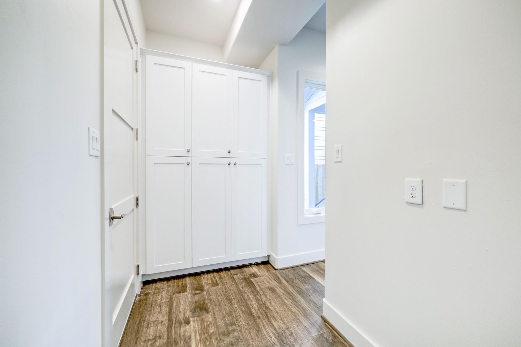 3827 Arlington Street Houston, TX 77018 - Photo 15 of 39 Hallway with sleek wood flooring, white walls, and ample storage space with built-in cabinets. A window provides natural light, enhancing the welcoming ambiance.