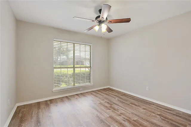 an empty room with wooden floor chandelier fan and windows