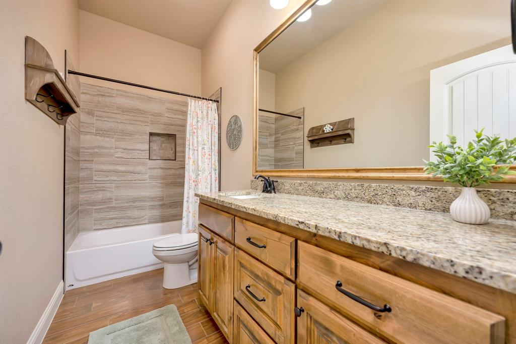 3224 North Cardinal Road Azle, TX 76020 - Photo 26 of 40 Bathroom featuring a wood-finish vanity with a stone countertop, a large mirror with sconce lighting, and a tiled shower/tub combination with a built-in niche