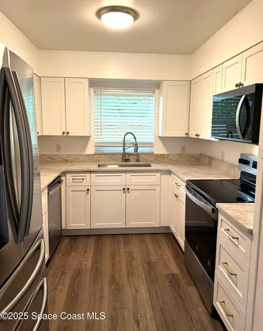 a white kitchen with stainless steel appliances granite countertop a stove a sink dishwasher and white cabinets with wooden floor