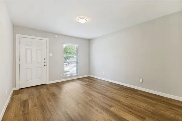 a view of an empty room with wooden floor and window