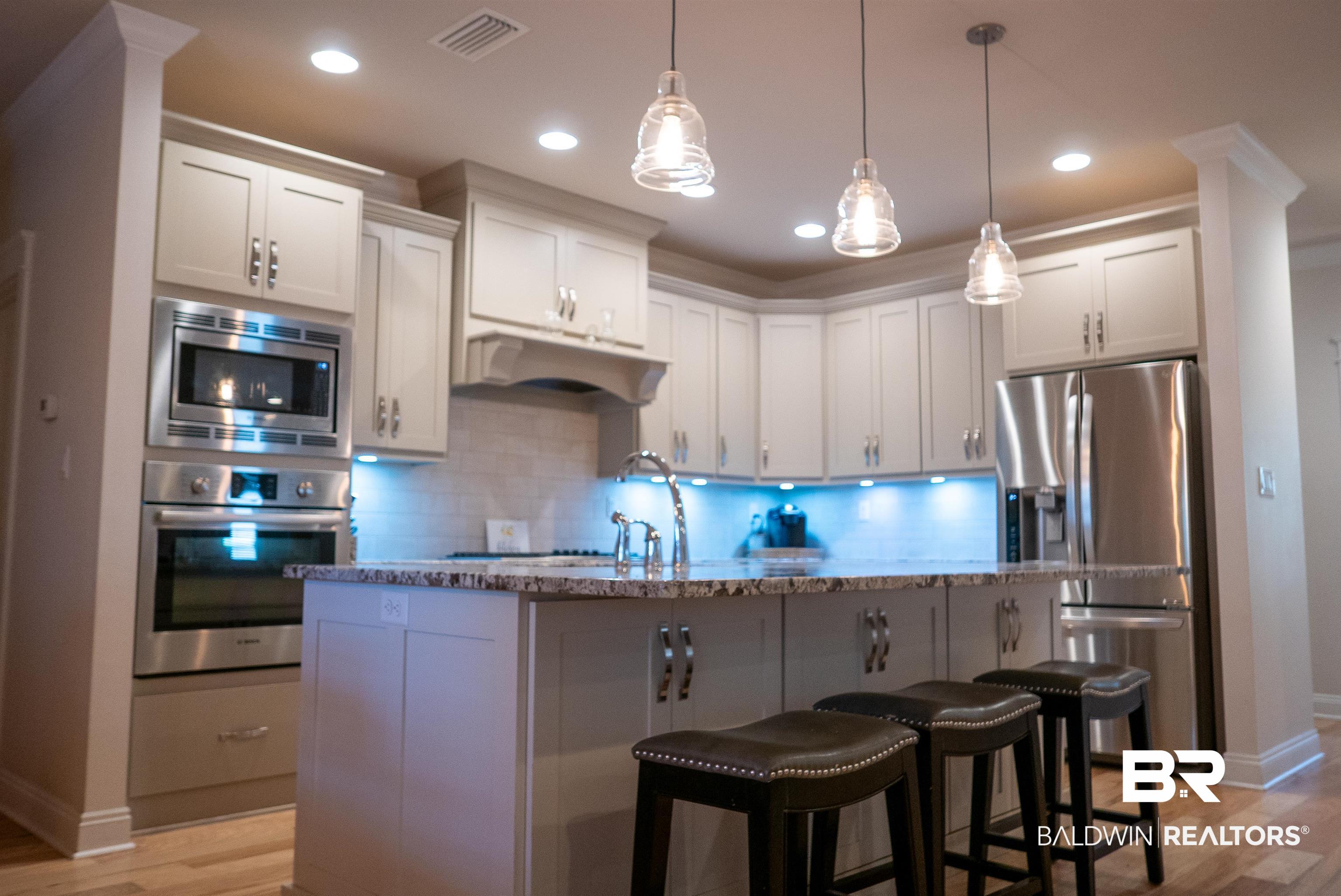6684 Garrison Drive Daphne, AL 36527 - Photo 25 of 35 Kitchen featuring light wood-type flooring, stainless steel appliances, pendant lighting, white cabinets, and a kitchen island with sink