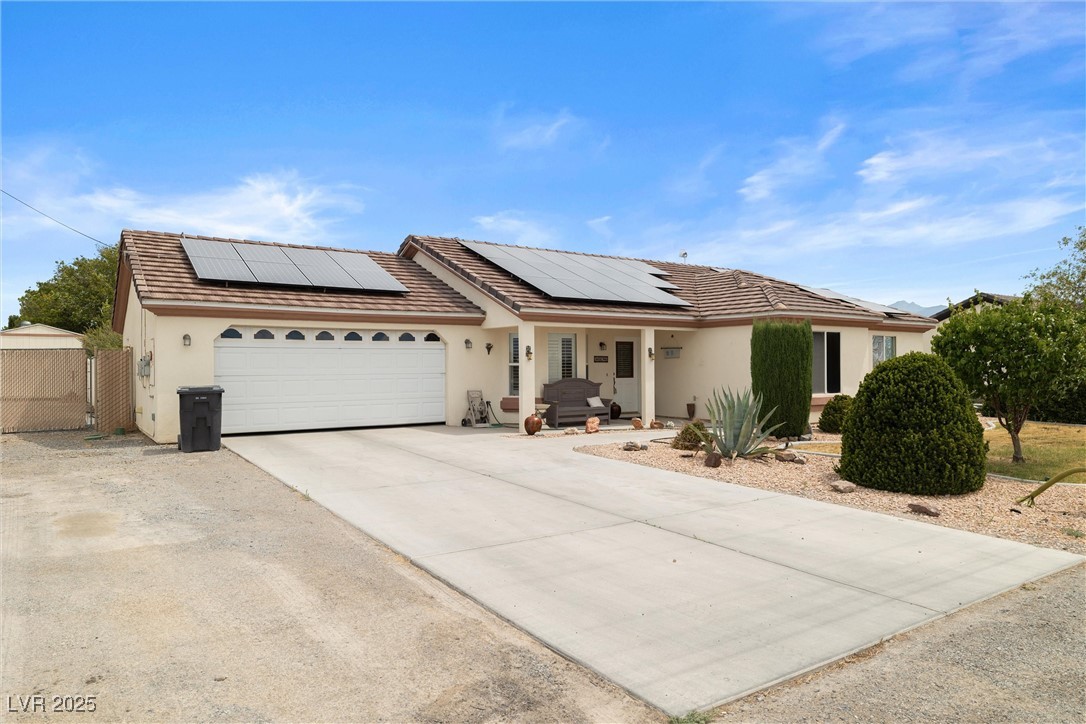 180 West Wilson Road Pahrump, NV 89048 - Photo 6 of 33 Ranch-style home featuring stucco siding, a garage, roof mounted solar panels, covered porch, and concrete driveway