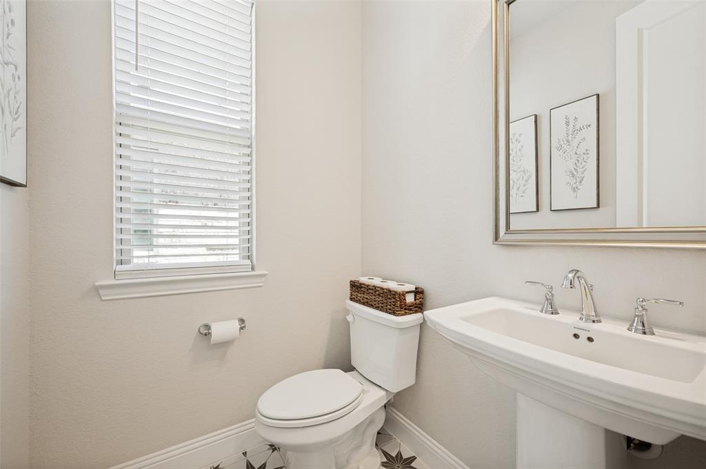 8440 Colburn The Colony, TX 75056 - Photo 15 of 34 Convenient first-floor powder bath featuring a classic pedestal sink, elegant framed mirror, and decorative tile flooring. A window provides natural light, creating a bright and welcoming space for guests.