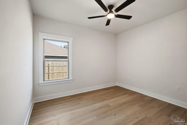 an empty room with wooden floor ceiling fan and windows