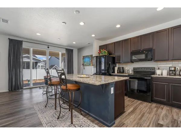 a kitchen with stainless steel appliances granite countertop a stove top oven a sink dishwasher a dining table and chairs with wooden floor
