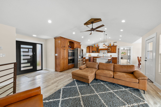 2591 East Washington Dam Road Washington, UT 84780 - Photo 6 of 67 Open-concept living area featuring wood-finish flooring, a contemporary ceiling fan, recessed lighting, a modern entry door with frosted glass, and a kitchen with warm wood cabinetry and an island with seating