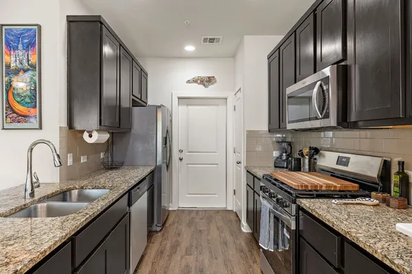 a kitchen with granite countertop stainless steel appliances a sink stove refrigerator and cabinets