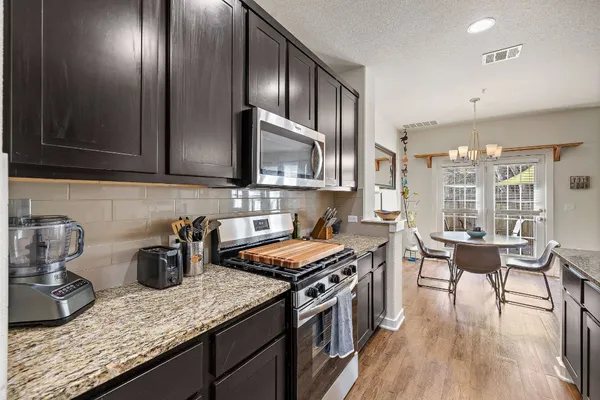 a kitchen with stainless steel appliances granite countertop a stove a sink dishwasher a microwave oven and a dining table with wooden floor