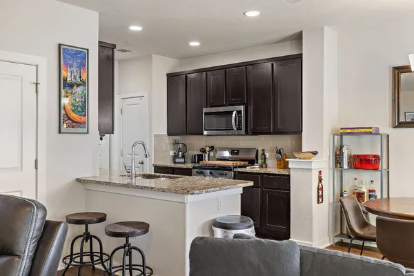 a kitchen with stainless steel appliances granite countertop a stove top oven a sink dishwasher and a refrigerator with wooden cabinets