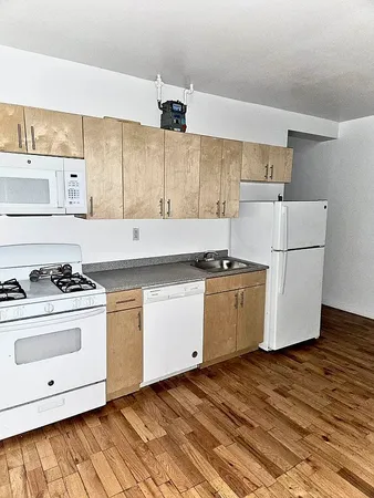 a kitchen with granite countertop a white stove top oven and white cabinets with wooden floor
