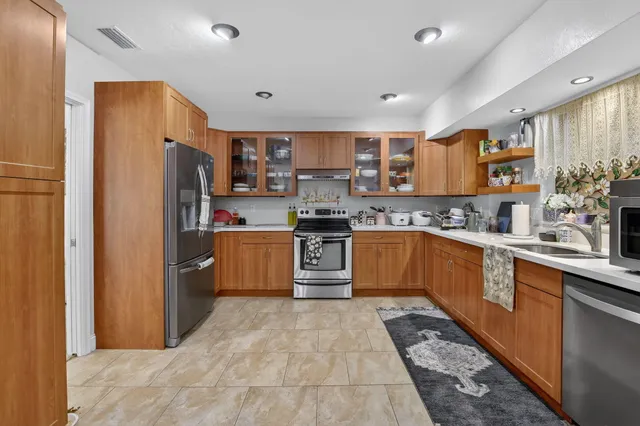 a kitchen with stainless steel appliances kitchen island granite countertop a refrigerator a sink a stove with white cabinets and wooden floor