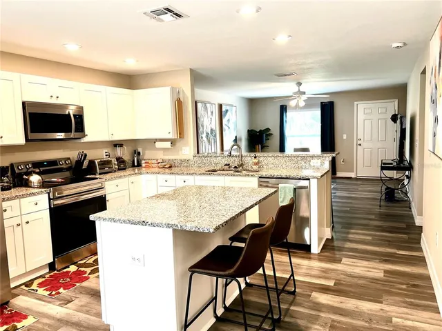 a kitchen with stainless steel appliances granite countertop a stove top oven a sink a dining table and chairs with wooden floor