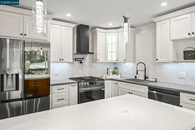 a kitchen with stainless steel appliances granite countertop a stove top oven a sink a refrigerator and white cabinets with wooden floor