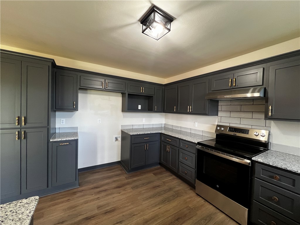 213 Carter Road Pottsville, AR 72858 - Photo 10 of 41 Kitchen featuring dark cabinetry, granite-style countertops, wood-finish LVP flooring, stainless steel range, and a subway tile backsplash