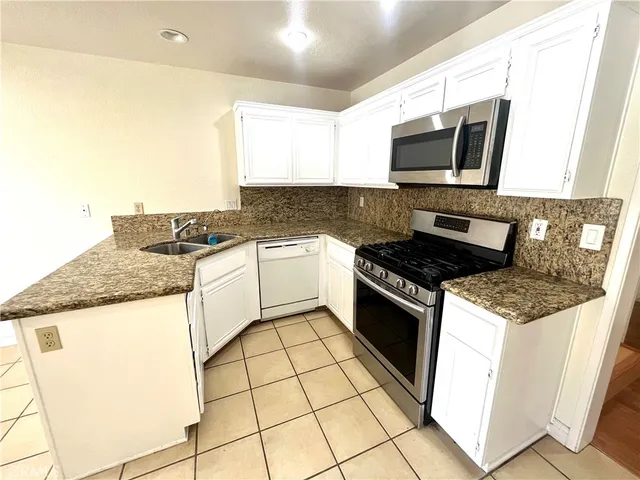 a kitchen with granite countertop a sink a stove top oven and cabinetry