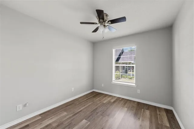 an empty room with wooden floor window and ceiling fan