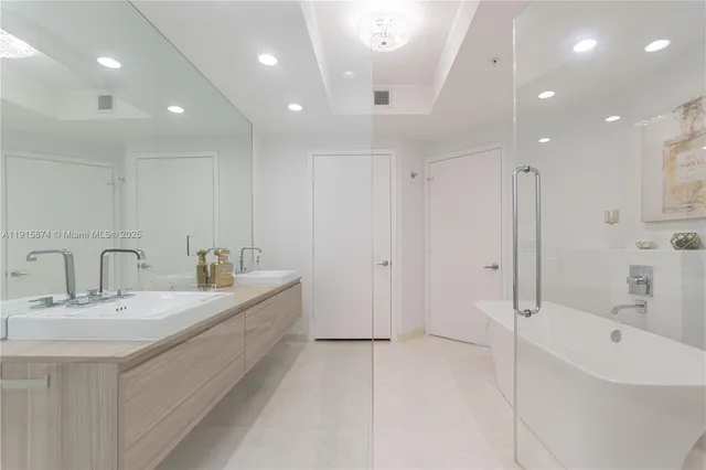 a large white bathroom with a double vanity sink a mirror and a bathtub