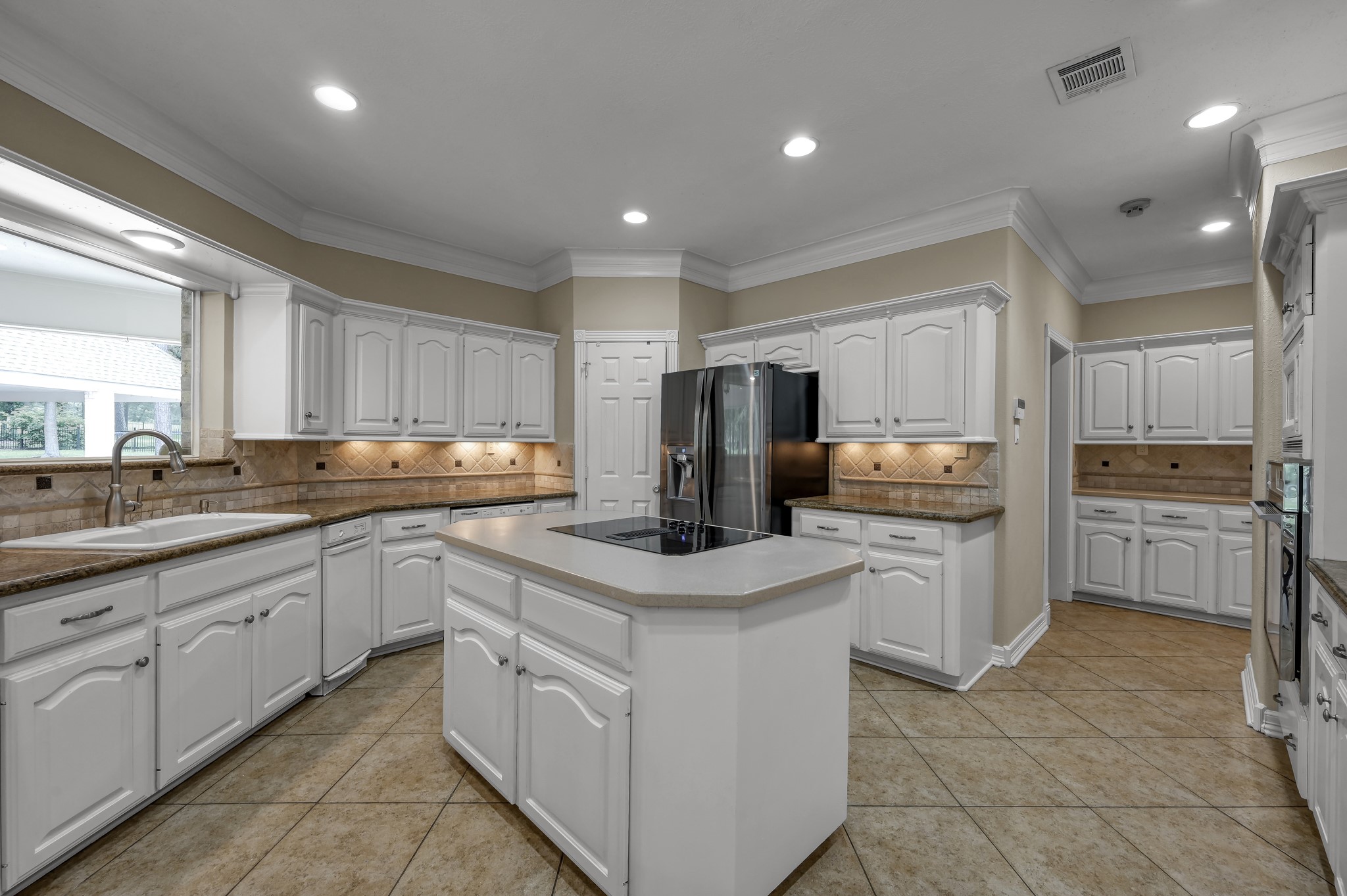 2205 Longmire Road Conroe, TX 77304 - Photo 13 of 49 This spacious kitchen features white cabinetry, and a central island with an electric cooktop. The room is well-lit with recessed lighting and offers a neutral color palette, creating a warm and inviting atmosphere for cooking and entertaining.