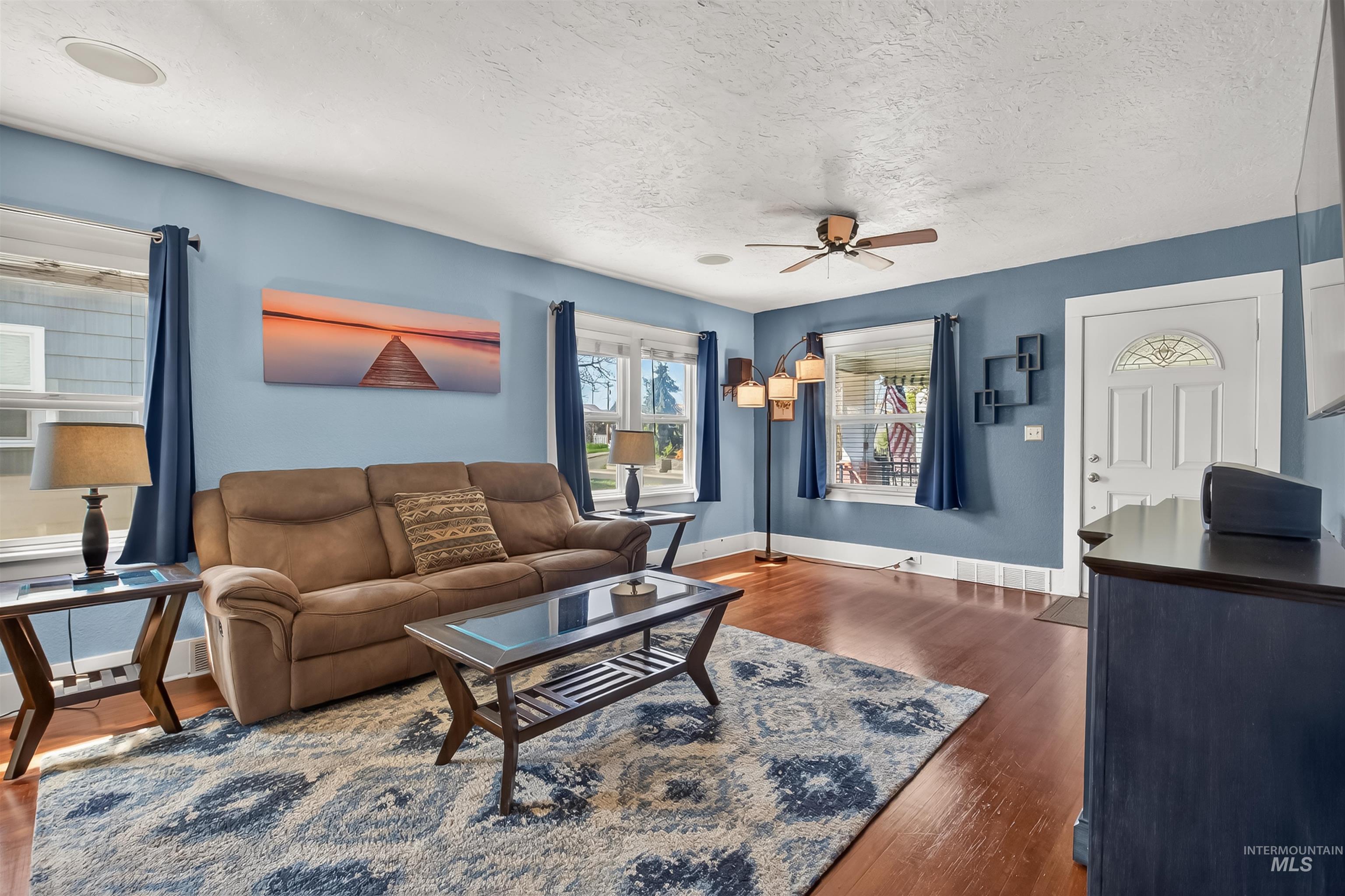 Living room featuring ceiling fan, dark wood finished floors, and a textured ceiling