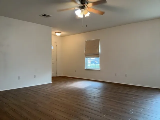 an empty room with wooden floor chandelier fan and windows