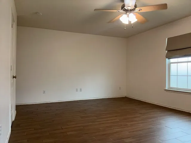 an empty room with wooden floor fan and windows