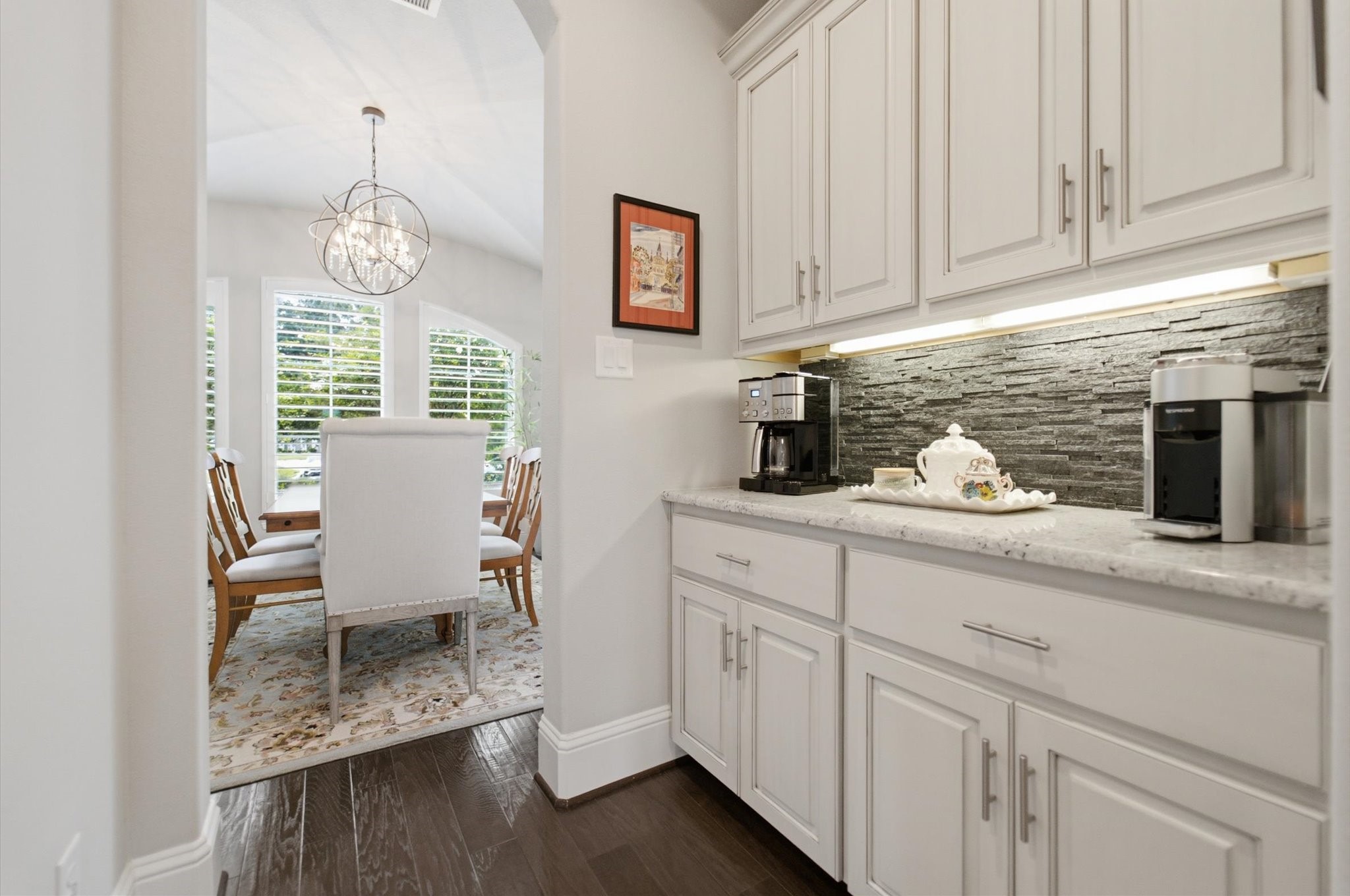 23722 Thortons Park Lane Spring, TX 77389 - Photo 16 of 48 This photo showcases a bright dining area with large windows and a modern light fixture, connected to a stylish butler's pantry featuring white cabinetry, a stone backsplash, and ample countertop space for coffee and appliances.