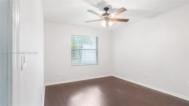 an empty room with wooden floor window and ceiling fan
