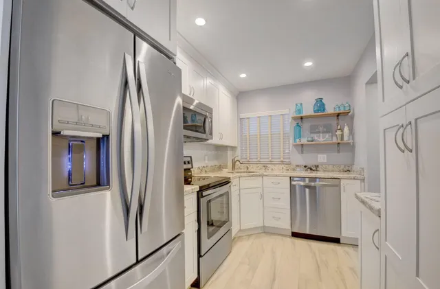 a kitchen with stainless steel appliances granite countertop a refrigerator a stove a sink and white cabinets with wooden floor