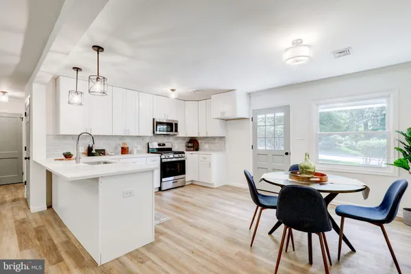 a kitchen with stainless steel appliances kitchen island a table chairs and a refrigerator