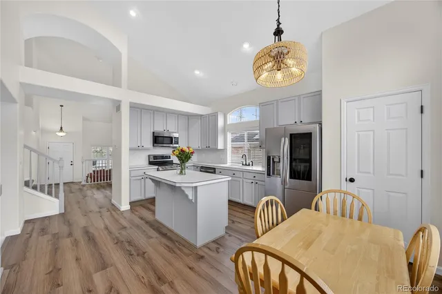 a kitchen with stainless steel appliances granite countertop a stove top oven a refrigerator a sink dishwasher a dining table and chairs with wooden floor