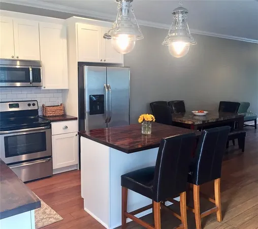 a kitchen with stainless steel appliances granite countertop a stove top oven a refrigerator a dining table and chairs with wooden floor