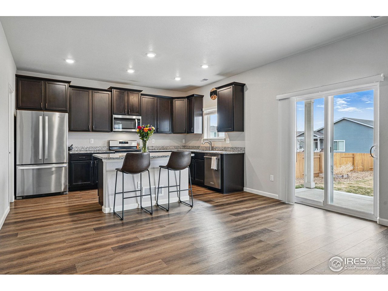 2310 Angus Street Mead, CO 80542 - Photo 13 of 39 a open kitchen with kitchen island a stove a refrigerator a sink and a dining table with wooden floor