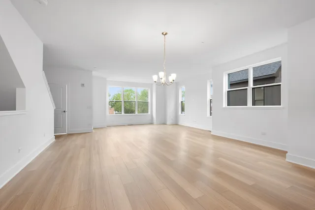 an empty room with wooden floor chandelier and windows