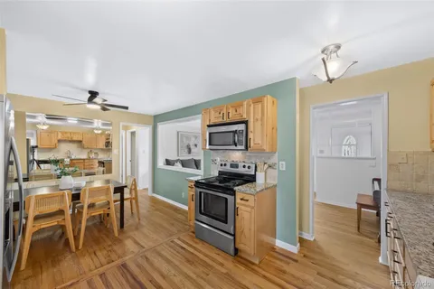 a kitchen with stainless steel appliances a stove top oven a sink a dining table and chairs with wooden floor